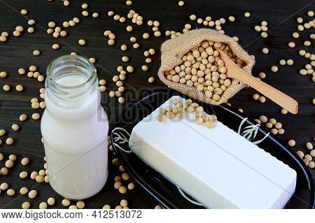 Bottle Of Soy Milk And Plate Of Tofu On The Table With Blurry Soybeans Scattered From Burlap Bag