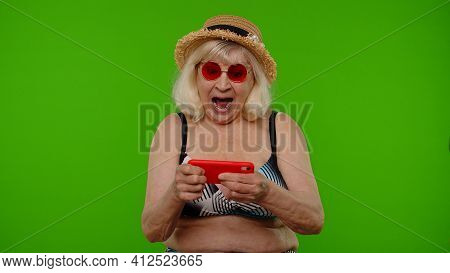 Senior Old Exited Woman Tourist In Swimsuit Playing Video Game On Mobile Cell Phone On Chroma Key