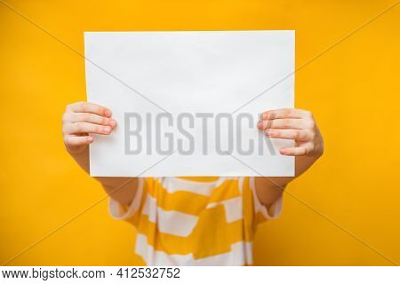 Kid Boy Holding White Blank Banner Over His Face, Standing Isolated On Yellow Background. Advertisem