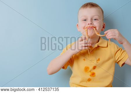 Portrait Of A Child Eating Spaghetti With Hands. Boy Stained With Tomato Sauce. Isolated On Blue Bac