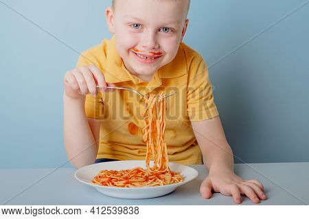 Cute Boy Eating Spaghetti Bolognese At Home. Concept Of Dirty Stains On Clothes. Isolated On Blue Ba