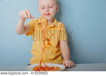 Cute Boy Eating Spaghetti Bolognese At Home. Concept Of Dirty Stains On Clothes. Isolated On Blue Ba