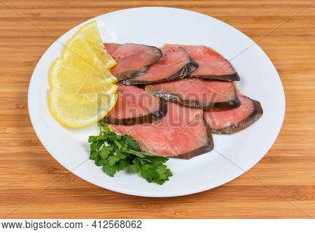 Slices Of Smoked Pink Salmon On Skin With Lemon Slices And Parsley Twig On Dish On A Wooden Surface