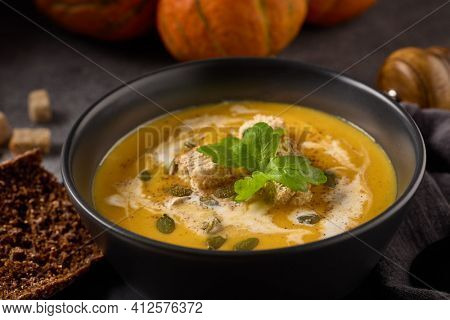 Pumpkin cream soup with pumpkin seeds and dried bread cubes. Lenten menu. Healthy, vegetarian food. Bowl with soup  and orange pumpkins on gray background.