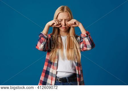 Blonde young upset woman crying and rubbing her eayes isolated over blue background