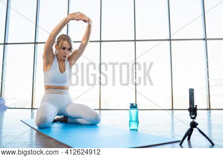 Girl Warming Up While Sitting On Yoga Mat In Front Of The Camera Phone. Female Sports Blogger Record