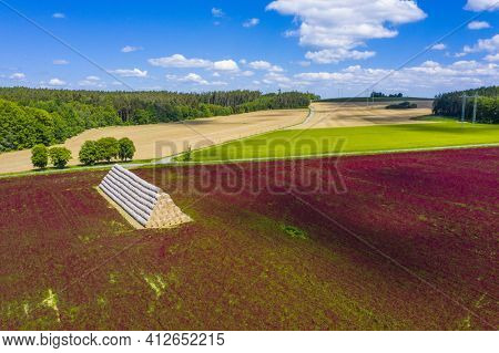 Red blooming crimson clover field (Trifolium incarnatum) and heap of bales seen from above
