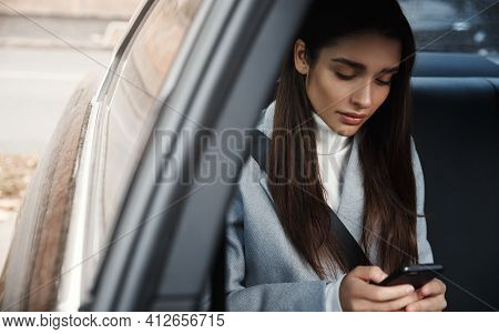 Elegant Woman Sitting On Backseat Of Her Car And Reading Message On Mobile Phone. Businesswoman Wear