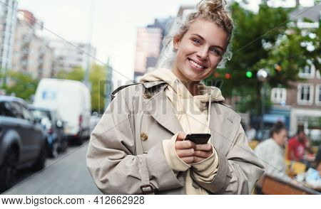Smiling Happy Woman Standing On Street With Mobile Phone. Beautiful Blond Girl Waiting For Cab, Orde