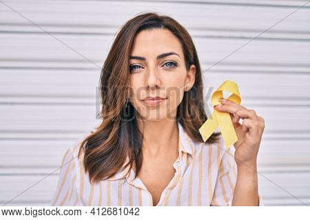 Young hispanic woman with serious expression holding awareness yellow ribon standing at the city.