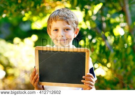 Happy Little Kid Boy With Chalk Desk In Hands. Healthy Adorable Child Outdoors Empty Desk For Copysp