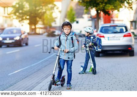Two School Kid Boys In Safety Helmet Riding With Scooter In The City With Backpack On Sunny Day. Hap
