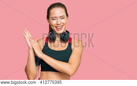 Beautiful blonde woman wearing gym clothes and using headphones clapping and applauding happy and joyful, smiling proud hands together 