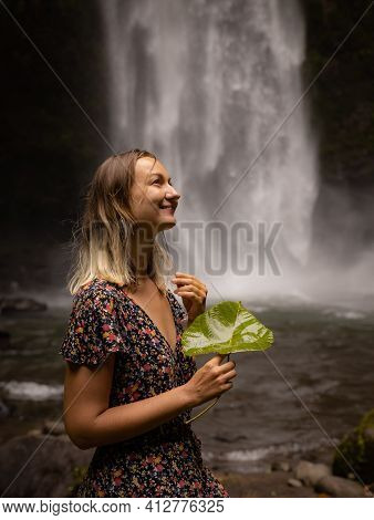 Caucasian Woman Holding Leaf, Enjoying Waterfall Landscape. Nature And Environment Concept. Travel L