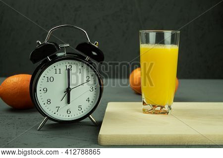 Alarm Clock At Which Six O'clock In The Morning. Black Clock And Orange Juice. Time - 6:00 Am And Re