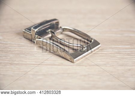 Square Nickel Plated Buckle With Flat Tongue On A Wooden Background.