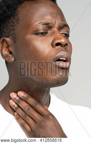 Black Man Touches Fingers Of Sore Throat, Thyroid Gland Isolated On Gray Background. Painful Swallow