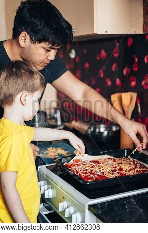 Father And Son Sprinkle Grated Cheese On Pizza. Preparing For The Mothers Day Holiday. Asian Father 