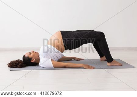 Young Flexible Pregnant Woman Doing Gymnastics On Rug On The Floor On White Background. The Concept 