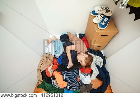 Lazy Boy Lying On The Thrown Clothes On The Floor. Mess In Open Wardrobe. Untidy Clutter Clothing Cl