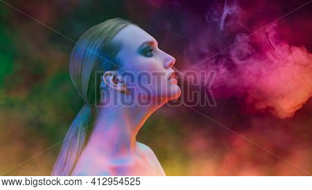 Art portrait of a gorgeous woman with dark make-up smoking in red light on a dark background with mixed lighting. Smoking hookah.