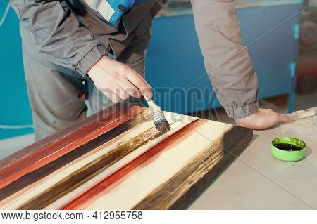 A Working Cabinetmaker Holds A Brush In His Hand And Paints A Wooden Surface. A Trace Of Paint On A 