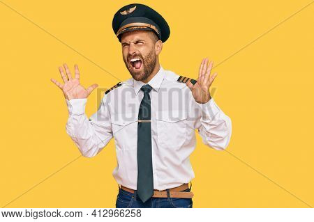 Handsome man with beard wearing airplane pilot uniform celebrating mad and crazy for success with arms raised and closed eyes screaming excited. winner concept 