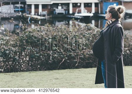 Side View Of Very Pregnant Blone Woman Taking A Walk By River Or Lake