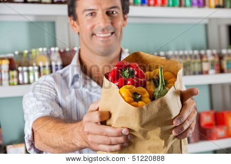 Portrait of mid adult male customer showing bellpeppers in paper bag at supermarket
