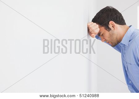 Angry man with fist clenched leaning his head against a wall