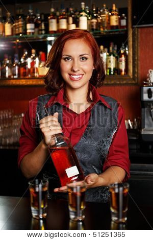 Beautiful redhead barmaid making shots