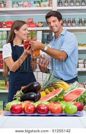 Portrait of mid adult male customer with saleswoman comparing bellpepper at supermarket