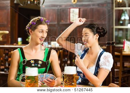 In Pub - friends in Tracht, Dirndl and Lederhosen drinking a fresh beer in Bavaria, Germany playing cards
