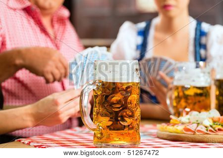 In Pub - friends in Tracht, Dirndl and Lederhosen drinking a fresh beer in Bavaria, Germany playing cards