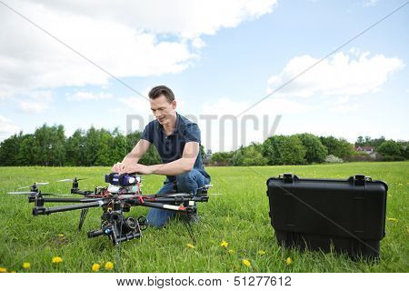 Young engineer crouching while fixing photography UAV in park