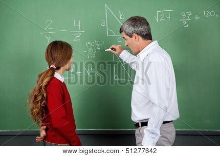 Side view of male professor teaching mathematics to female student on board in classroom