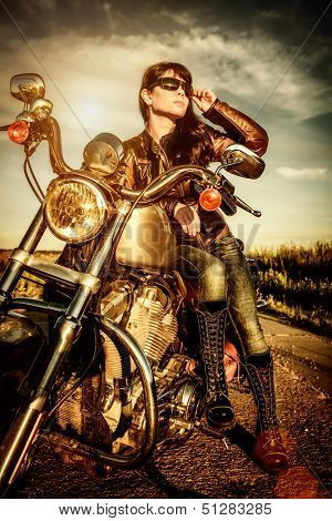 Biker girl in a leather jacket on a motorcycle looking at the sunset.