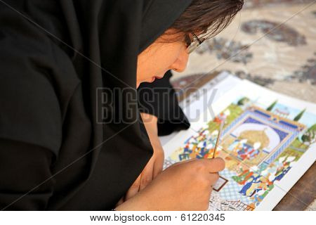 ESFAHAN, IRAN - DECEMBER 01, 2007: Muslim woman artist in black headscarf paints traditional Persian miniature