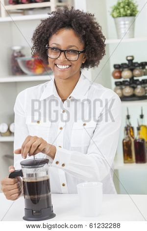 A beautiful happy mixed race African American girl or young woman making coffee with a cafetiere in her kitchen at home