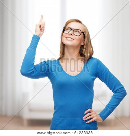advertisement concept - attractive young woman in casual clothes and black eyeglasses pointing her finger up