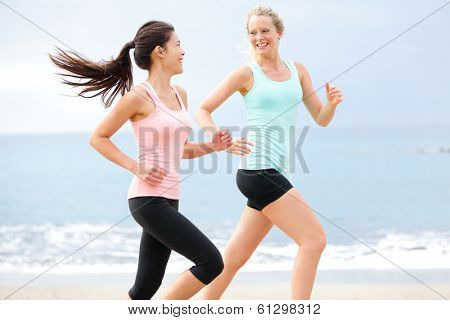 Exercise running women jogging happy on beach training as part of healthy lifestyle. Two fit female runners talking happy and smiling during workout. Multiracial Asian and Caucasian woman.
