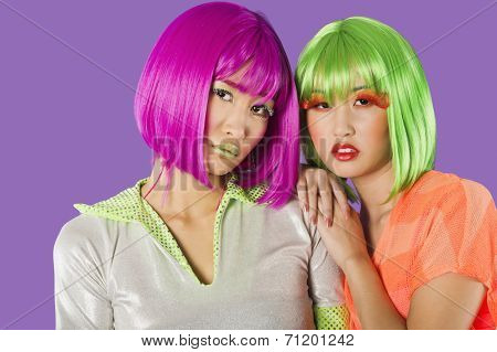 Portrait of two female friends wearing wigs against gray background