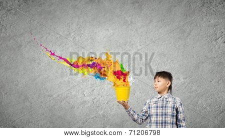 Young boy splashing colorful paint from bucket