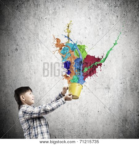 Young boy splashing colorful paint from bucket