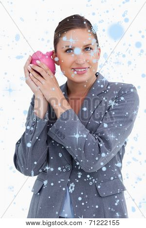 Smiling bank clerk shaking piggy bank against snow falling