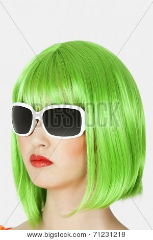 Young woman wearing green wig over gray background