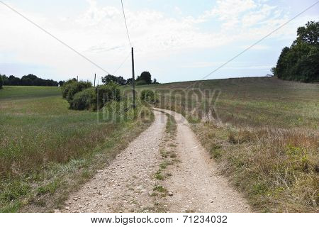 Unpaved road in grassy field against cloudy sky