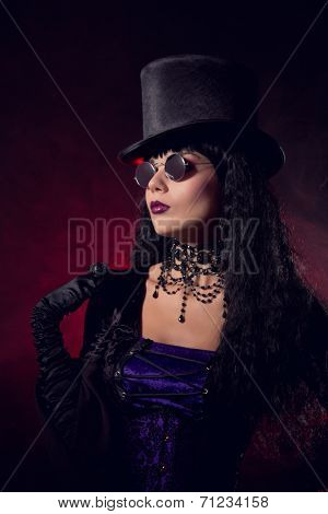 Vampire gothic girl in tophat and round eyeglasses, studio shot with smoke background 