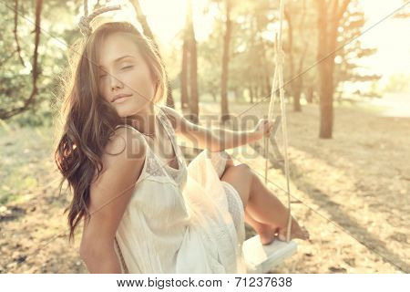 Young woman is swinging on a swing in summer pine forest. Image toned and noise added.