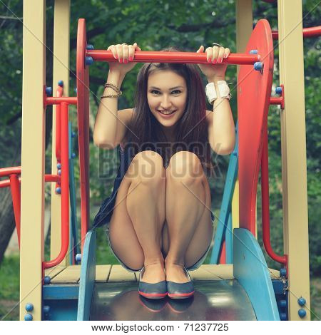 Happy teen girl has fun  on child hillock on playground. Outdoors. Image toned and noise added.